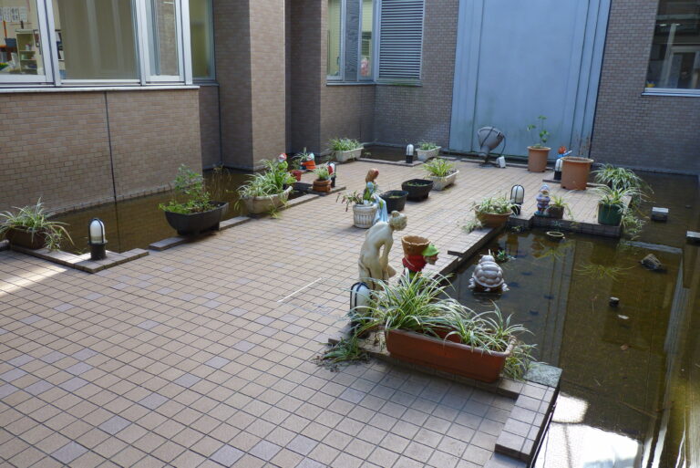 介護施設の中庭。レンガ張りの広場に植栽やオブジェが配置された共有外構スペース