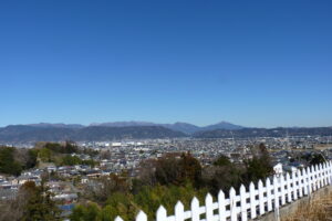 施設から見える周辺の住宅地と山並みの眺望。白いフェンスが手前に見える